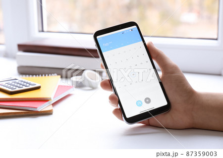 Woman using calendar app on smartphone indoors, closeup 87359003