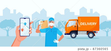 Delivery man with medical protective mask on his face holding package with yellow truck on background. Delivery during quarantine time. Safe shipping order. Online delivery app on phone screen 87360565