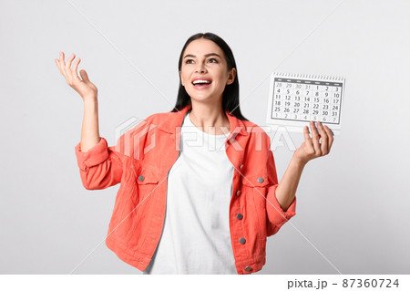 Emotional young woman holding calendar with marked menstrual cycle days on light background Emotional young woman holding calendar with marked menstrual cycle days on light background 87360724