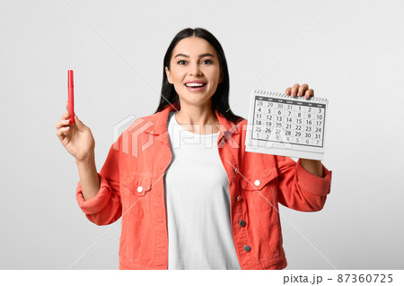Young woman holding calendar with marked menstrual cycle days on light background Young woman holding calendar with marked menstrual cycle days on light background 87360725