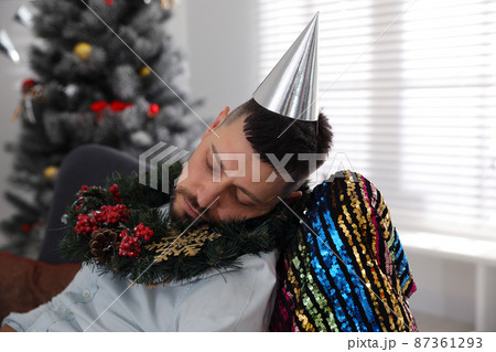Drunk man with festive cap and wreath sleeping in room after New Year party Drunk man with festive cap and wreath sleeping in room after New Year party 87361293