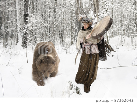 Shaman woman playing on shaman frame drum in a winter forest 87362043