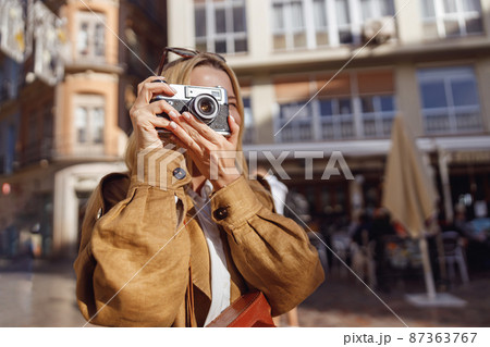 Portrait of smiling woman holding retro camera looking at viewing slot 87363767