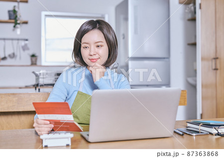 預金通帳を笑顔で見つめるエプロン姿の若い女性 87363868