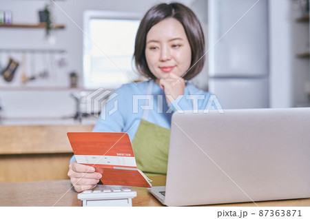預金通帳を笑顔で見つめるエプロン姿の若い女性 預金通帳を笑顔で見つめるエプロン姿の若い女性 87363871