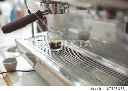 Close up of glass cup with coffee standing on grate of coffee machine 87363878