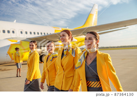 Joyful women flight attendants walking down airfield 87364130