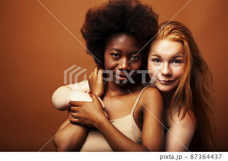 young pretty african and caucasian women posing cheerful together on brown background, lifestyle diverse nationality people concept 87364437