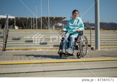 A caucasian woman in a wheelchair cannot go down stairs without a ramp. Hard to access environment. A caucasian woman in a wheelchair cannot go down stairs without a ramp. Hard to access environment. 87364571