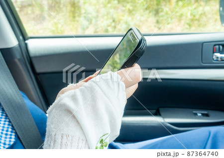 車の助手席でスマートフォンを見る女性の写真。スマホ依存症のイメージ。 車の助手席でスマートフォンを見る女性の写真。スマホ依存症のイメージ。 87364740