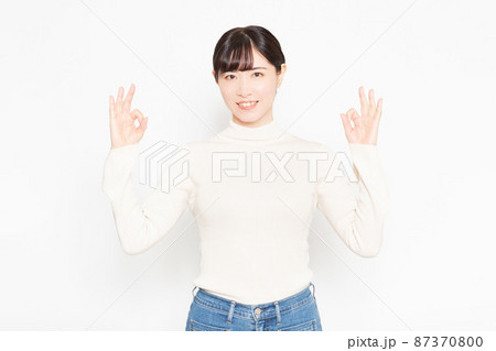 白い背景の前に立ってOKのジェスチャーをする女性 87370800