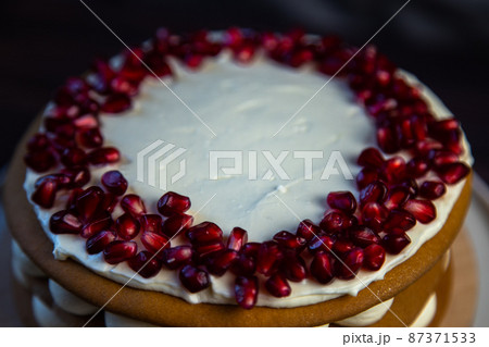 Cake with sponge cakes, decorated with white cream and pomegranate seeds on top in a circle, layers of cream are visible in circles on the side, a close-up view from the side. High quality photo Cake with sponge cakes, decorated with white cream and pomegranate seeds on top in a circle, layers of cream are visible in circles on the side, a close-up view from the side. High quality photo 87371533