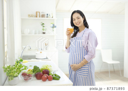 キッチンでオレンジジースを飲む妊婦 87371893