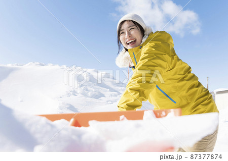 笑顔で雪かきをする若い女性 87377874