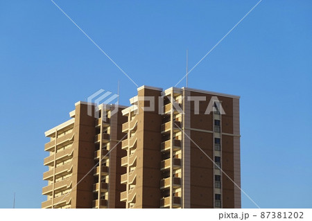 青空をバックに立方体型で外階段2本のマンションが1棟建っている風景 87381202