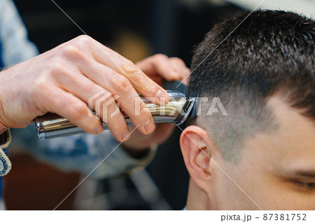 hairdresser makes a haircut of nape for a man with a hair clipper in barbershop 87381752