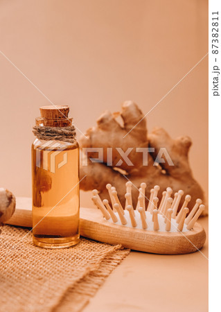 Glass bottle of essential ginger oil, ginger root on beige background. Healthy alternative living. Natural cosmetics ingredients for hair care. Wellness Eco comb Homemade hair mask treatment 87382811