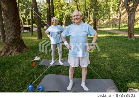 Sportive mature man and woman train on mats on lush lawn Sportive mature man and woman train on mats on lush lawn 87383903