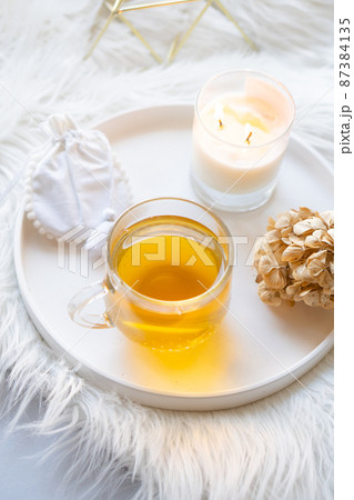 Cup of herbal tea and burning candle on round white decorative tray Cup of herbal tea and burning candle on round white decorative tray 87384135