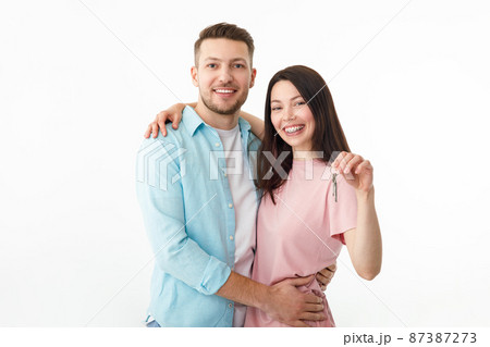 A cheerful young couple is hugging in the kitchen, holding the keys to a new house in their hands. Happy newlyweds moved into a new apartment, got a mortgage, moving day. A cheerful young couple is hugging in the kitchen, holding the keys to a new house in their hands. Happy newlyweds moved into a new apartment, got a mortgage, moving day. 87387273