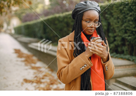 Young black woman in a coat drinking coffee outside 87388806