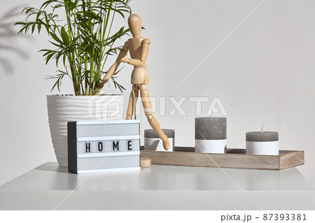 Table, gray different sized candles on wooden stand, figurine of human, lamp with inscription home, green plant in pot. Isolated on white. Close up Table, gray different sized candles on wooden stand, figurine of human, lamp with inscription home, green plant in pot. Isolated on white. Close up 87393381