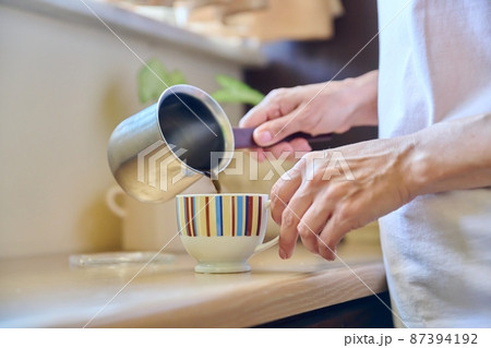 Close-up of a woman's hands preparing coffee in an iron cezve. 87394192