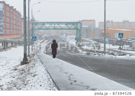 Snowy weather in the city. A woman walks along the snow-covered sidewalk. 87394526