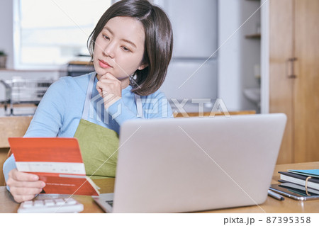 預金通帳を見つめて老後を考えるエプロン姿の若い女性 87395358