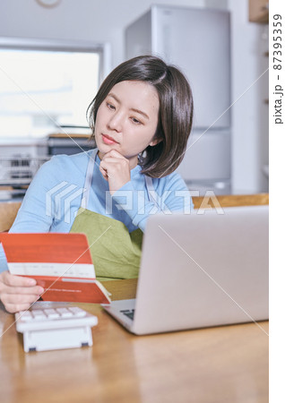 預金通帳を見つめて老後を考えるエプロン姿の若い女性 87395359
