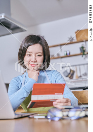 預金通帳を笑顔で見つめるエプロン姿の若い女性 87395368