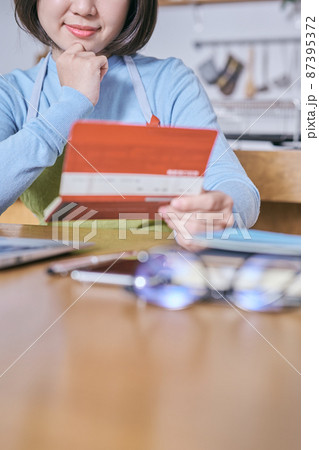 預金通帳を笑顔で見つめるエプロン姿の若い女性 預金通帳を笑顔で見つめるエプロン姿の若い女性 87395372
