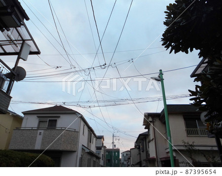 住宅街の空に張り巡らされた電線と電柱を見上げた風景 87395654