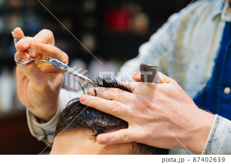 hairdresser makes a haircut for a brunet man with a scissors in a barbershop hairdresser makes a haircut for a brunet man with a scissors in a barbershop 87402639