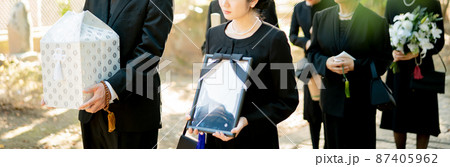お葬式・納骨式で遺骨と遺影を持って墓地を歩く遺族 87405962