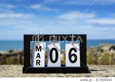 Mar 06 calendar date text on wooden frame with blurred background of ocean 87408483