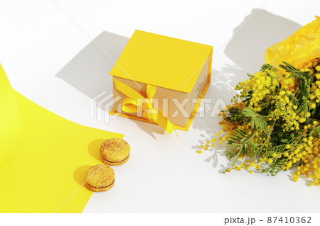 Branches of yellow mimosa flowers, french yellow macaroons and yellow gift box with ribbon bow. Greeting for International Womens Day on March 8, mothers day, Easter, Birthday or spring concept. 87410362