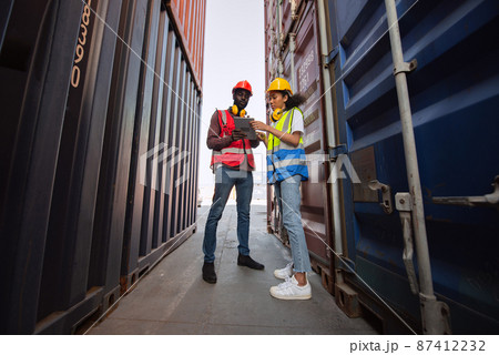 Two African american male and female worker using tablet and checking control loading freight containers from Cargo freight ship for import export. 87412232