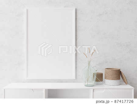 Empty vertical picture frame on white wall in modern living room. Mock up interior in minimalist, scandinavian style. Free space for picture. Console, rattan basket, dried grass in vase. 3D rendering. 87417726