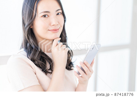 窓際でスマホを操作する若い女性 窓際でスマホを操作する若い女性 87418776