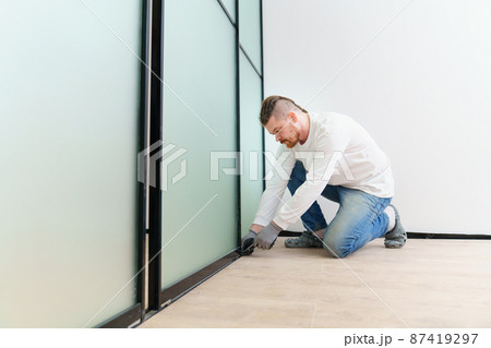 master adjusts sliding doors of wardrobe made of metal and glass. 87419297