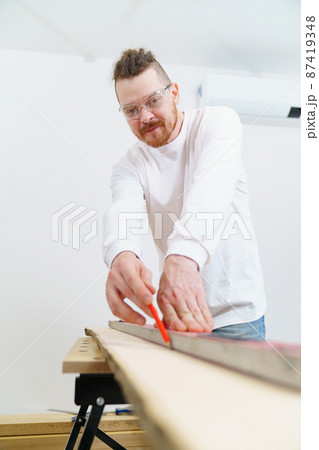 carpenter in protective gloves and glasses makes measurements and draws on wood carpenter in protective gloves and glasses makes measurements and draws on wood 87419348