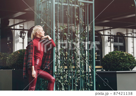 fashionable blonde girl with a red lipstick posing outdoors . Dressed in a red leather leggings, turtleneck and checkered jacket. fit figure fashionable blonde girl with a red lipstick posing outdoors . Dressed in a red leather leggings, turtleneck and checkered jacket. fit figure 87421138
