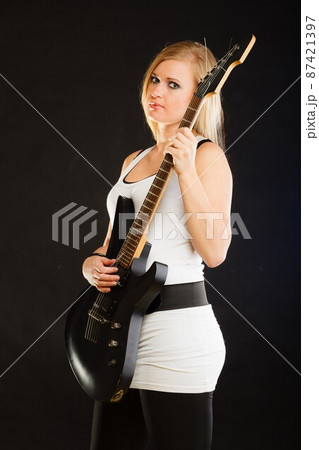 Blonde woman holding electric guitar, black background Blonde woman holding electric guitar, black background 87421397