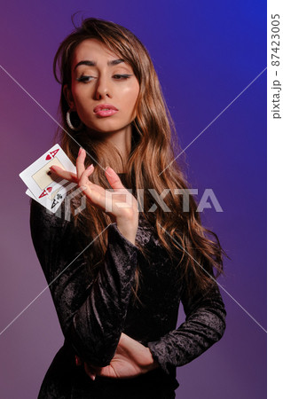 Brunette woman in black velvet dress showing two playing cards, posing against coloful background. Gambling entertainment, poker, casino. Close-up. Brunette woman in black velvet dress showing two playing cards, posing against coloful background. Gambling entertainment, poker, casino. Close-up. 87423005