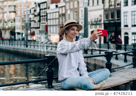 Cheerful woman taking selfie on bench during trip 87426211