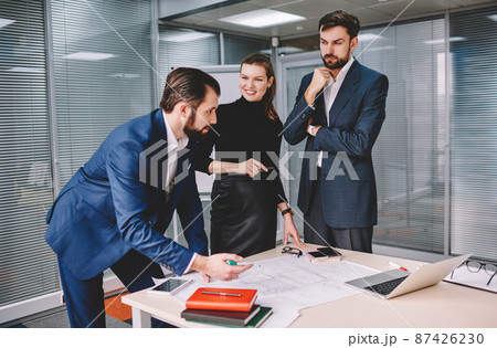 Smiling woman and male coworker attentively listening to confident coworker Smiling woman and male coworker attentively listening to confident coworker 87426230