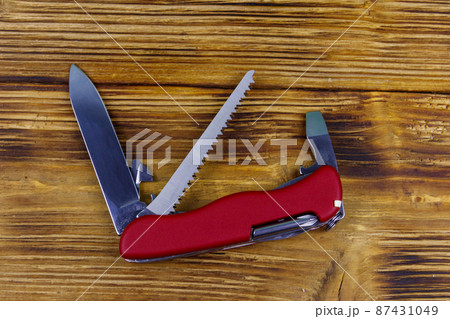 Red all purpose pocket knife on a rustic wooden background. Top view Red all purpose pocket knife on a rustic wooden background. Top view 87431049