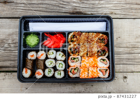 Set of sushi rolls in plastic box on wooden table. Sushi for take away or delivery of sushi in plastic container. Top view Set of sushi rolls in plastic box on wooden table. Sushi for take away or delivery of sushi in plastic container. Top view 87431227