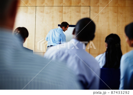 Executive giving presentation while peers watch. Rear view of group of people looking at executive giving presentation. Executive giving presentation while peers watch. Rear view of group of people looking at executive giving presentation. 87433292